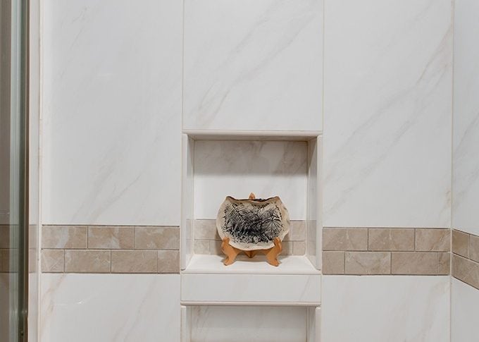 white tile shower showing recessed soap area with brown tile accent